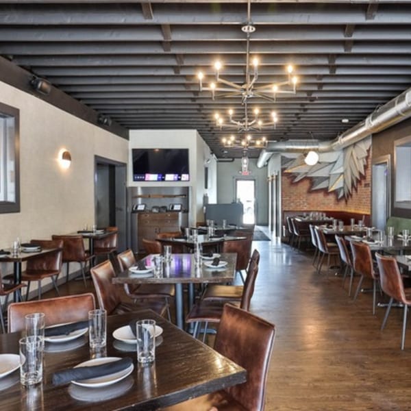 The Brookdale restaurant interior with set tables, leather chairs, exposed brick, and modern chandeliers.