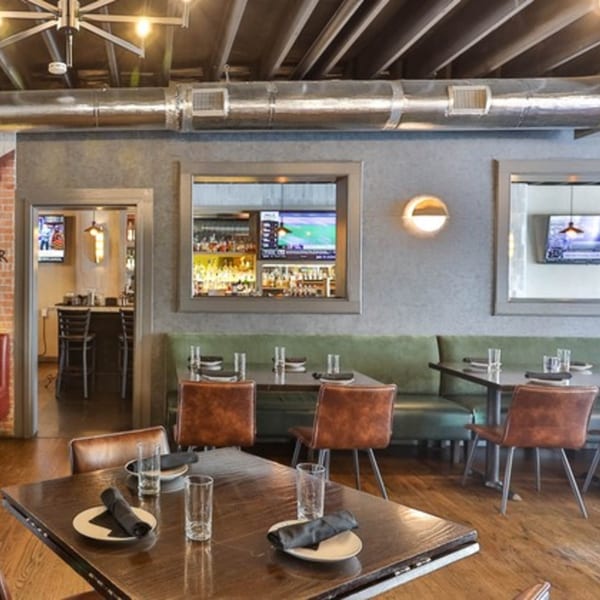 The Brookdale's dining room with tables, brown chairs, green booths, and a view into the bar area.
