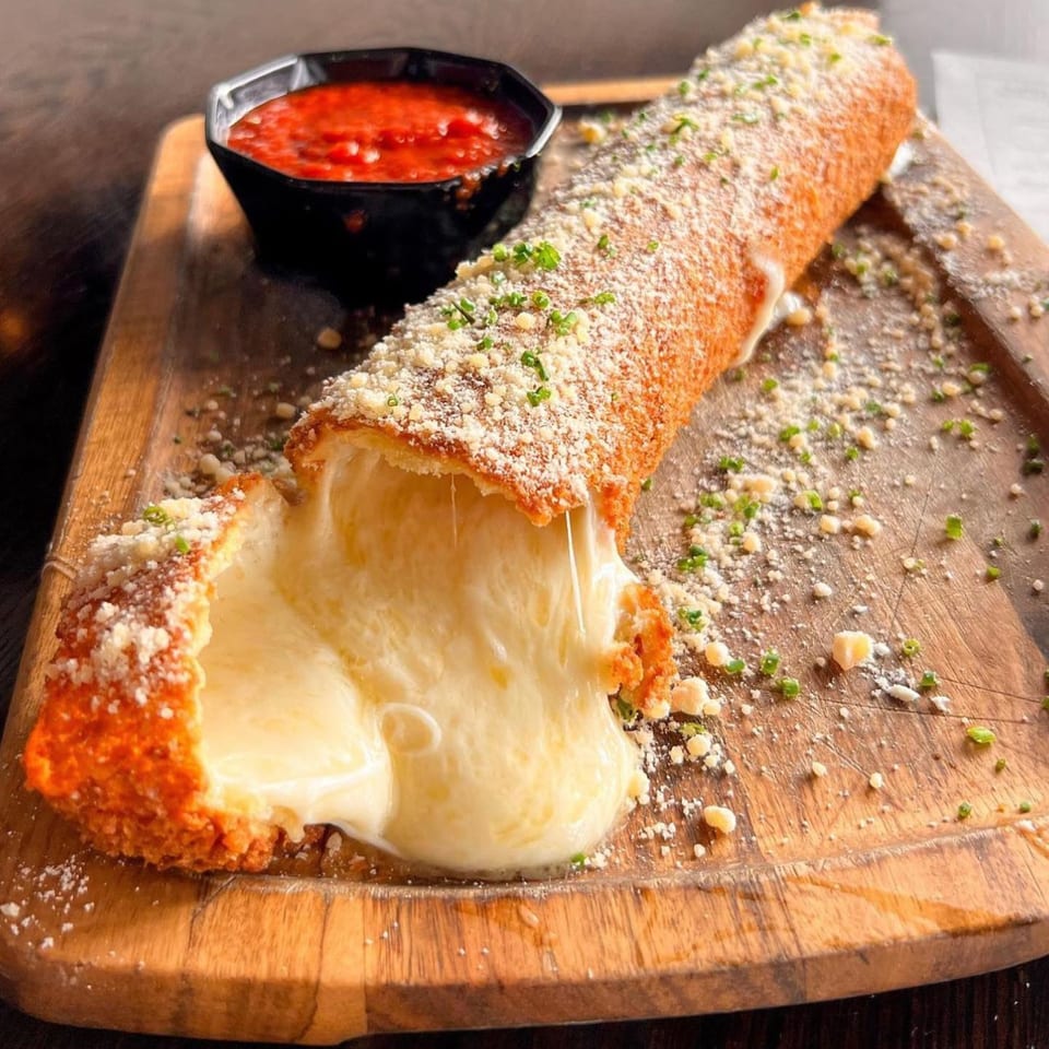 A giant mozzarella stick, broken open with melted cheese oozing out, served with marinara sauce.