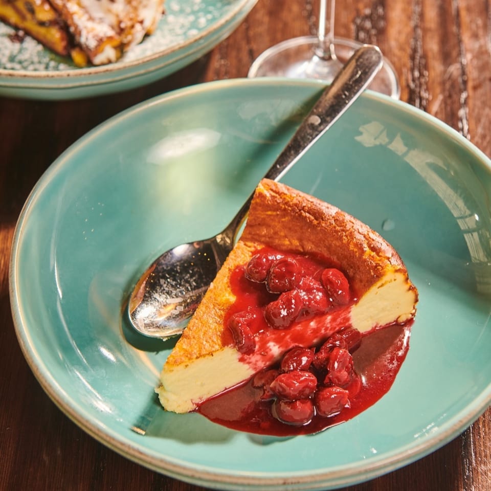A slice of cheesecake with cherry topping and a spoon on a teal plate.