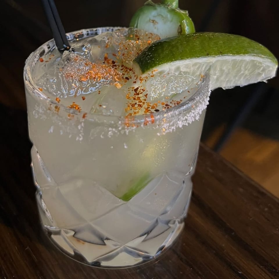 A Brookdale margarita with a salted rim, lime wedge, and chili flakes on a wooden table.